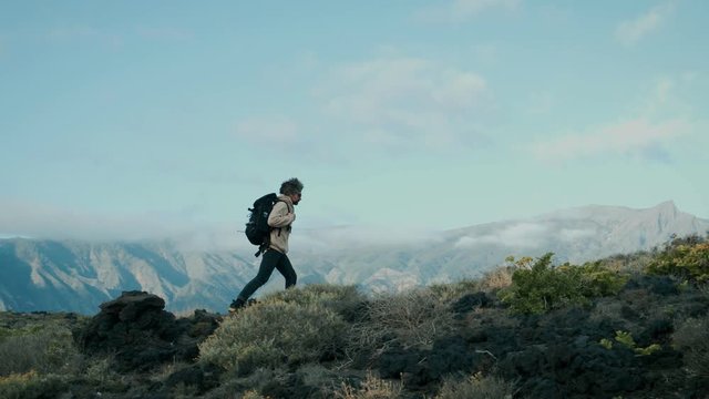 Epic inspiring video of motivating middle aged man or adult male during exploration hike or camping trip climbs up mountain ridge in incredible natural landscape on sunny day, adventures ahead