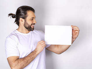 handsome man in white t-shirt over white background, shows white sheet of paper