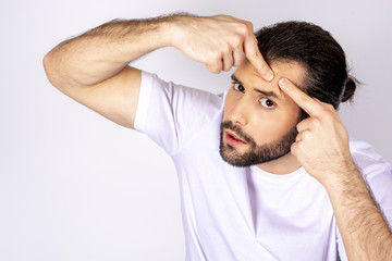 Handsome man in a white T-shirt on a white background, squeezes pimples on his face