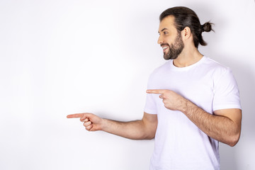 A handsome man in a white T-shirt on a white background, shows a finger to the side