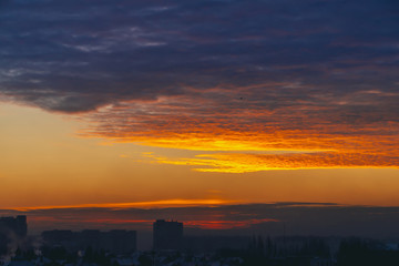 Cityscape with wonderful varicolored fiery dawn. Amazing dramatic multicolored cloudy sky. Dark silhouettes of city building roofs. Atmospheric background of sunrise in overcast weather. Copy space.