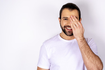 handsome man in white t-shirt over white background, closes his eyes with his hand