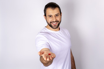 A handsome man in a white T-shirt on a white background, smiling, holding pills in his hand