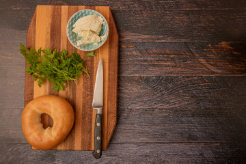 Fototapeta na wymiar Plain toasted bagel with cheese and herbs on wooden chopping board