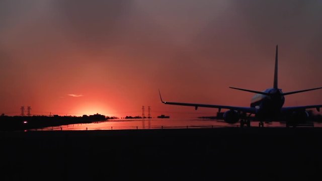 An airplane silhouetted against the sunset waits on a runway