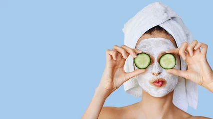Poster Schöne junge Frau mit Gesichtsmaske auf ihrem Gesicht, die Gurkenscheiben hält. Hautpflege und -behandlung, Spa, natürliche Schönheit und Kosmetikkonzept. © Olesia