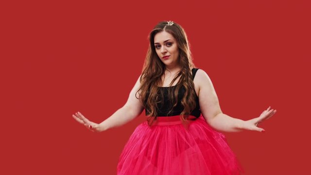 Camera moving up on beautiful plus size female in pink tutu stepping forward and looking at camera while striking pose on red background
