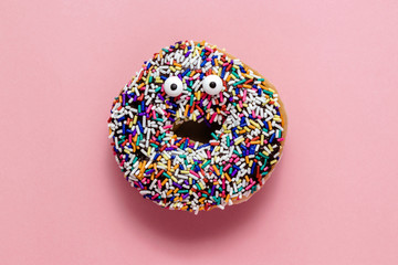 Funny shock face chocolate donut with sprinkles on a pastel pink background, creative minimal food concept, doughnut isolated on colorful background