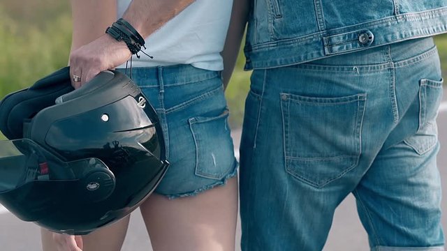 close view man hand with ring bracelets and helmet hugs lady waist in blue denim shorts and white t-shirt slow motion