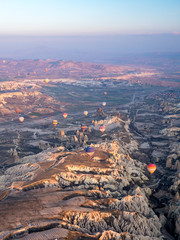 Obraz premium Colorful hot air balloons above Turkish National Park in Goreme. Panorama of Cappadocia landscape - multi colored balloons flying over mountain valley of ancient cave town Uchisar. March, 2019