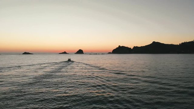 AERIAL: Sunrise over water at Hahei Beach past fishing boat 2