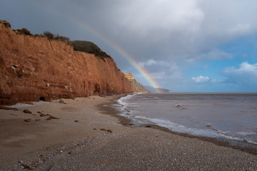 A rainbow touches down on a deserted Sidmouth beach in Devon, England