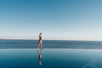 girl in a swimsuit walks along the edge of the panoramic pool