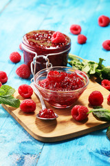 raspberry jam with fresh raspberries and mint. marmalade on spoon and jar on blue