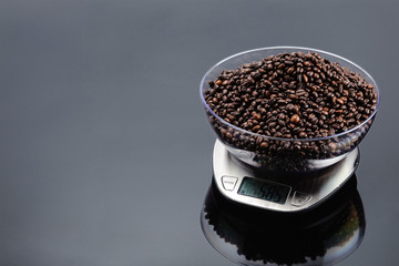Coffee beans in bowl on an electronic scale on grey mirror background with copy space