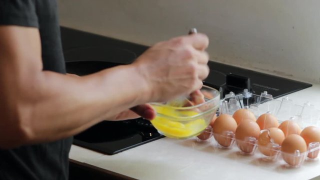 man beating eggs in a glass bowl near ceramic stove top in kitchen