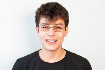 The teenager in glasses sincerely smiles on a light background and on the teeth has braces
