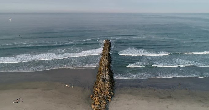 Surfers on the beach near a rock jetty.