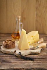 Two types of cheeses - parmesan and gouda with walnuts and honey on wooden board with cheese knives