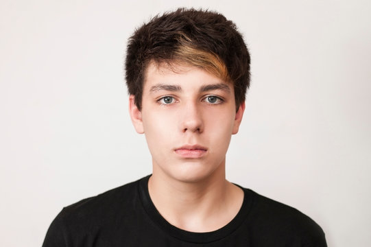 A beautiful but sad boy in a black shirt on a light background. The boy has painted hair and beautiful eyes