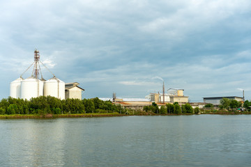 large industrial factory and silo building at side coast of sea in evening with cloudy sky