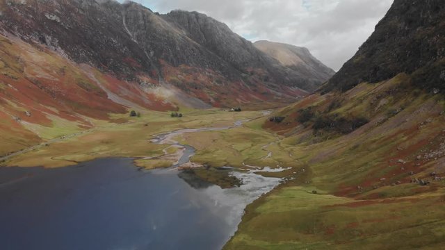 Slowly flying above a highland valley and lake surrounded on either side by Scottish mountains in the Glencoe area of Scotland. Aerial, 4K UHD.