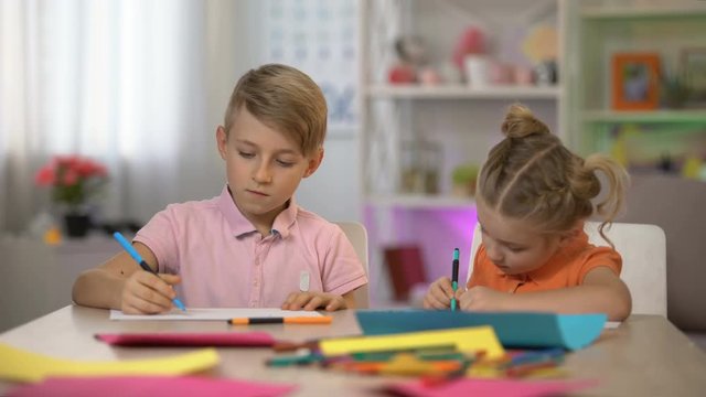 Adorable boy and girl drawing by pencils sitting at table, kindergarten leisure