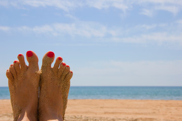 Female tanned legs with a bright pedicure on the sandy beach, a symbol of summer beach holidays. 