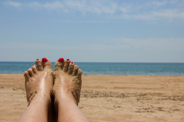 Female tanned legs with a bright pedicure on the sandy beach, a symbol of summer beach holidays. 