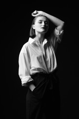 Portrait of an elegant young woman in a white shirt and black pants. Interesting studio light