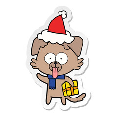 sticker cartoon of a dog with christmas present wearing santa hat