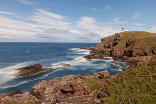 Stoer Head lighthouse on clifftop in a long  exposure with cloudy sky.