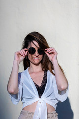 Front view of a beautiful trendy young woman wearing sunglasses standing in the street while posing to camera in a sunny day