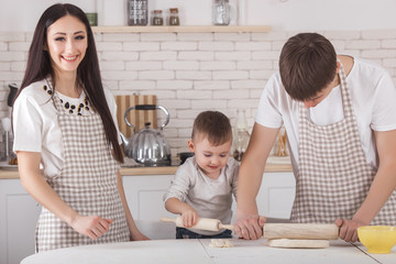 Adorable family cooking togrther. Young family in the kitchen having breakfast or dinner. Mom, dad and their little child preparing meal.