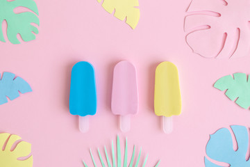Ice cream on stick with multicolored origami tropical leaves abstract on pastel pink.