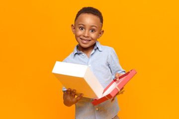 Portrait of surprised astonished cute little boy with dark black skin holding open box of birthday...
