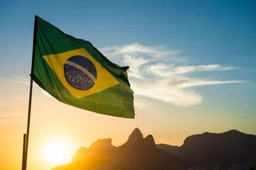 Papier Peint photo Brésil Brandir le drapeau brésilien en contre-jour devant les toits de la montagne au coucher du soleil doré sur la plage d& 39 Ipanema à Rio de Janeiro, Brésil
