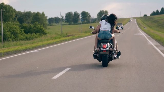 wonderful couple rides modern black motorbike between green trees and meadows against cars slow motion