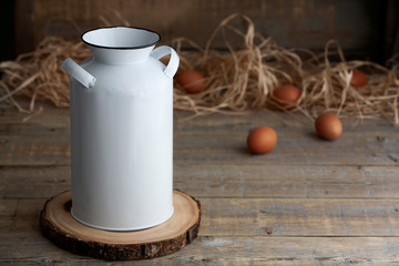 Mockup of a white vintage milk jug next to fresh eggs and straw on a brown wooden table.