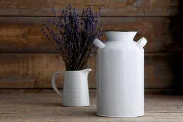 Mockup of a white vintage milk jug next to a vase of lavender on a brown wooden table.