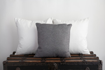 Mockup of grey square cushion with two white square cushions sitting on top of an old vintage suitcase.