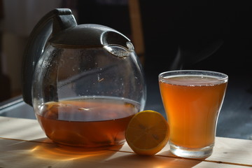 smoke rising from a cup of ginger tea with a teapot on a wooden table in front of a black background