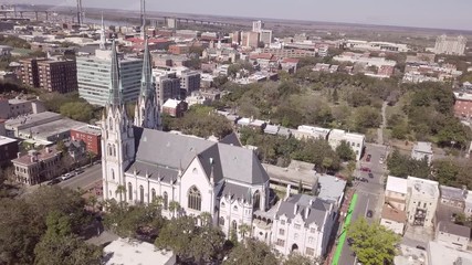 Aerial circling shot of St Johns Cathedral in downtown Savannah, Georgia with city center in background.