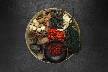 Mix composition of various exotic dried spices in natural bamboo bowl on black stone background