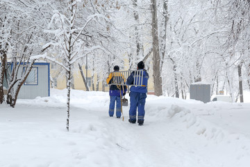 Two workers in blue uniform carry a ladder along the road in the snow in winter in Moscow