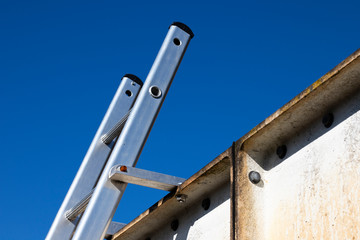 Aluminium ladder securely fastened at top to steelwork to comply with UK health and safety regulations