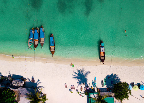 Aerial view of a young woman with a brazilian flag on the beach. Crystal clear water, tropical vacation scenario, coconut tree and boats. Drone view