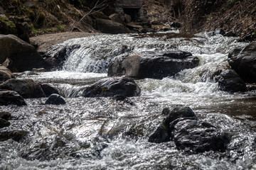 Small river on mountain swollen due to snow melt. Riverbed with big stones. End of winter and beginning of spring.