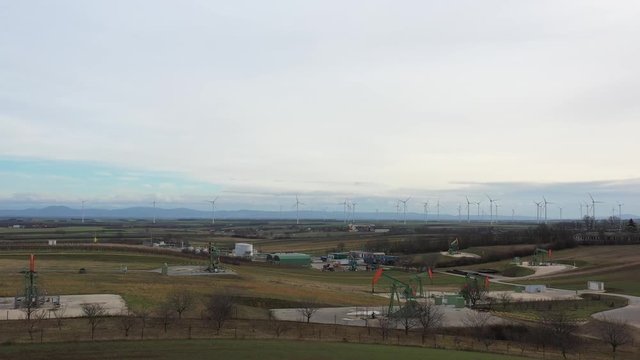 [DRONE]revealing shot of a scenery with multiple oil derricks moving and wind turbines in the background