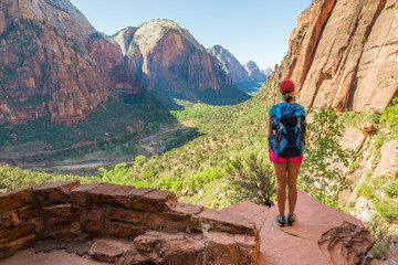 Young woman wearing backpack is looking at the view on the trail to Angel's Landing in Zion National park in Utah, USA. Female on a hiking trail in Zion National Park in Usa. - obrazy, fototapety, plakaty